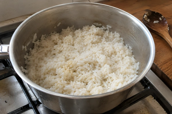 Par-cooked white rice in a stainless steel pot with water mostly absorbed.
