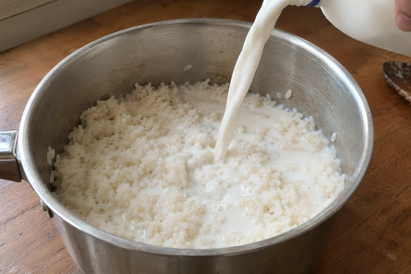 Fresh whole milk being poured over cooked rice in a saucepan