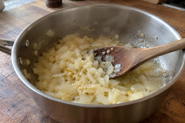 Finely diced onions and minced garlic cooking in melted butter inside a metal saucepan.