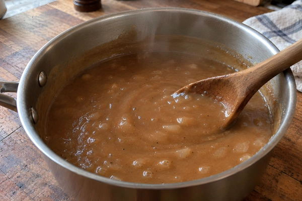 Smooth, thickened brown gravy simmered in a saucepan with a wooden spoon.