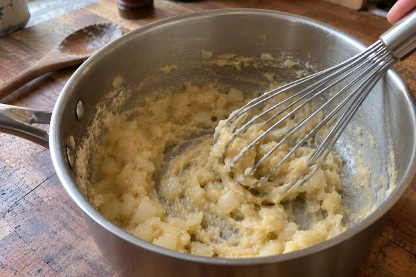 Whisking flour into sautéed onions and butter to form a thick roux base.