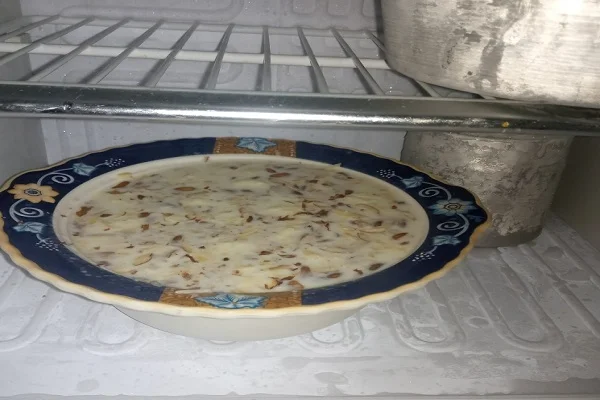 Shallow dish of ras malai resting on a refrigerator shelf for chilling