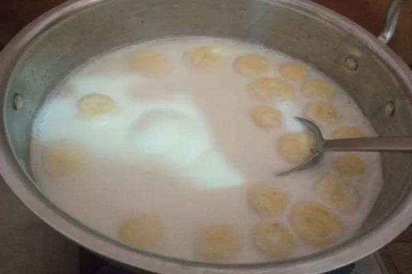 malai balls expanding while cooking in a wide pan of boiling milk