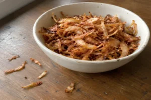 Thinly sliced onions fried to a deep golden brown crispness, piled high in a shallow ceramic dish.