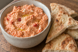 A bowl of creamy orange tirokafteri spicy feta dip served with warm pita bread triangles